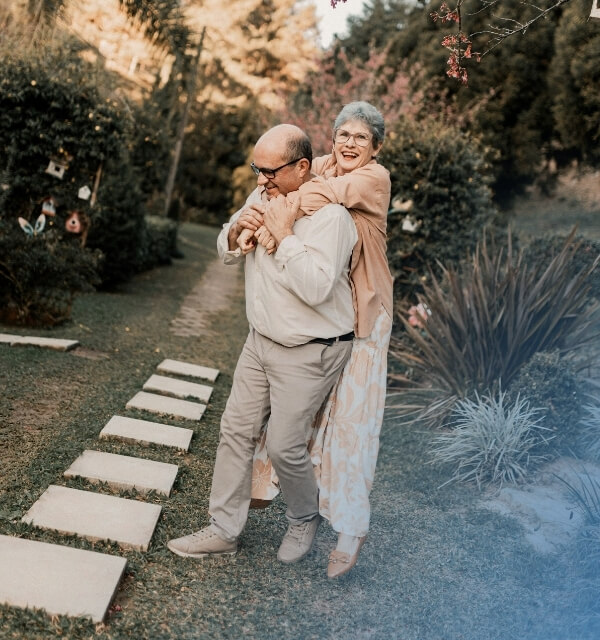 Pareja de adultos mayores sonríe durante un paseo en jardín